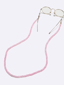Macro detail of pink beaded glasses chain with gold hardware on a minimalist background