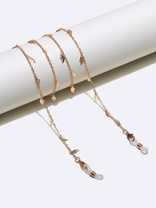 Detail of golden metal glasses chain featuring delicate leaf charms on a white pedestal