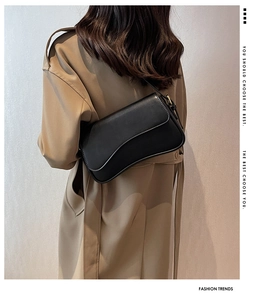 Detail of a minimalist black leather crossbody bag on a model wearing a khaki trench coat