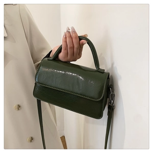 Detailed texture of dark green glossy leather and handle on a minimalist crossbody bag