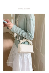 Detailed view of cream-colored textured handbag with knot handle and adjustable strap