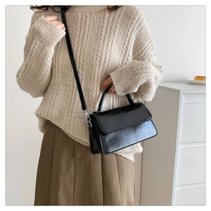 Glossy black leather crossbody bag styled with a beige sweater and brown skirt