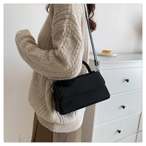 Classic black rectangular leather crossbody bag styled on a person in minimalist setting