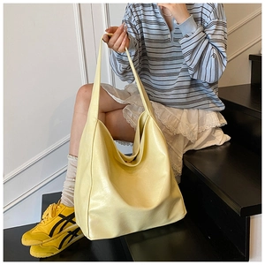 Detail view of large yellow leather tote bag with wide shoulder strap on casual model