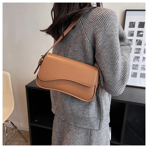 Brown faux leather shoulder bag with curved flap shown on model in minimal indoor setting
