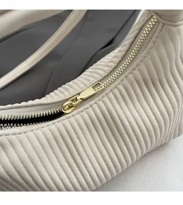 Close-up of smooth gold metal zipper and pleated faux leather texture on minimalist bag
