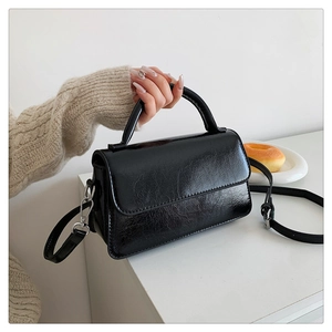 Detail of black glossy patent leather crossbody bag with pleated texture and silver hardware