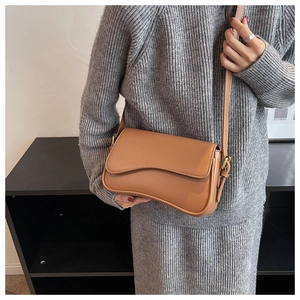 Side view of a light brown vintage crossbody bag with a wavy flap on a grey dress