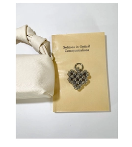Detailed macro view of silver beaded heart charm on a white leather handbag handle
