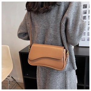 Detail of a brown leather crossbody bag with wavy flap design on a gray sweater