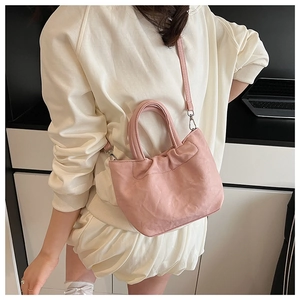Detailed view of a pink pleated dumpling bag worn crossbody with slim leather straps