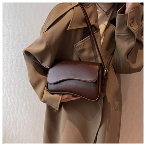 Detail of vintage brown shoulder bag with asymmetrical curved base on a khaki trench coat