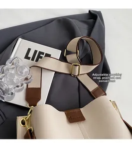 Detail of adjustable wide fabric shoulder strap on beige faux leather bucket bag