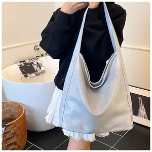 Detailed view of a silver large-capacity leather tote bag worn by a model in a modern room