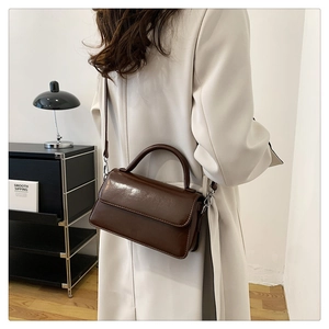 Detail view of a vintage dark brown leather crossbody bag styled with a cream-colored coat
