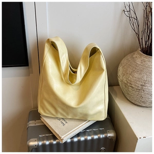 Detail of soft pale yellow PU leather tote bag placed on a vintage book and silver suitcase