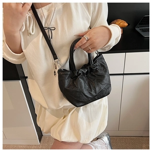 Fashionable black pleated cloud bucket bag shown on model with shoulder strap and round handle