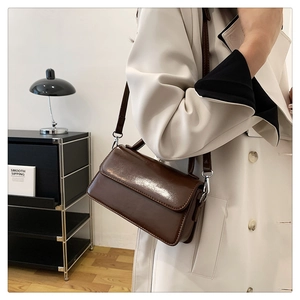 Detailed view of deep brown glossy crossbody bag with adjustable strap and metal hardware