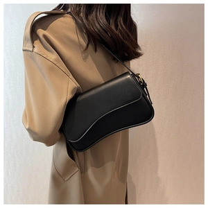 Detail of black leather underarm bag with gold metal hardware and sleek flap closure