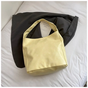 Detail of soft pale yellow large tote bag with glossy finish on elegant white bedding