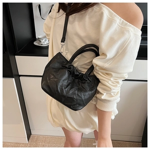Detail of black pleated leather crossbody bag with adjustable strap and top handles