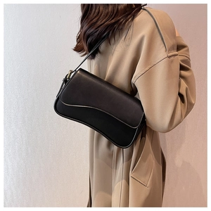 Detail of a vintage black leather shoulder bag with gold buckle on a beige trench coat
