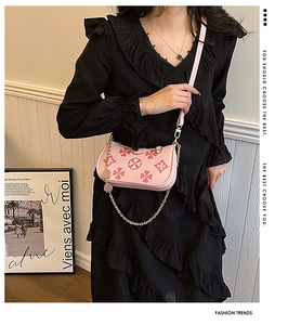 Detail of pink shoulder bag featuring clover prints and gold chain on a black dress