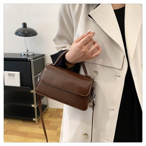 Detail of brown rectangular flap bag with smooth texture and detachable strap held by hand