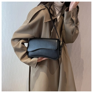Minimalist black crossbody bag with asymmetric flap shown on a trench coat model