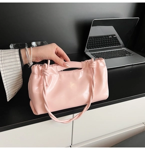 Detail view of pink glossy pleated cloud bag with thin strap in an office setting