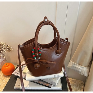 Détail du sac seau en cuir huilé marron avec nœud décoratif sur fond de livres d'art