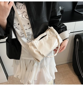 Detail of a creamy white glossy pleated shoulder bag with silver metallic buckles