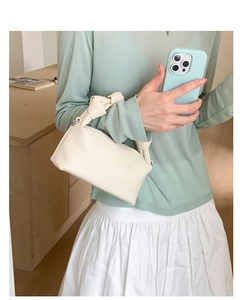 Detail of minimalist cream leather handbag featuring a stylish knot handle and litchi texture