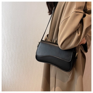Detail of a minimalist black leather shoulder bag with a wave flap and gold hardware