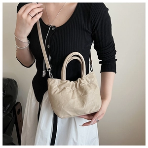 Detail of beige bucket bag with paper-like texture and adjustable shoulder strap on a model