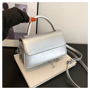 Detail of silver metallic textured crossbody bag with rigid handle and fine shoulder strap