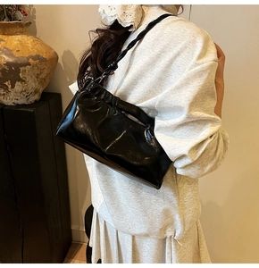Detail of black glossy pleated underarm bag with unique knotted strap and shiny finish