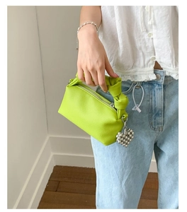 Detail of bright green textured leather handbag with knotted handle and heart charm