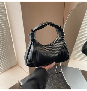 Detail of black pleated croissant bag with knotted handle and golden zipper detail