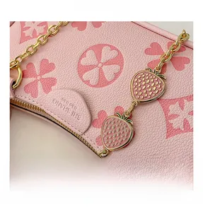 Detailed view of pink shoulder bag with strawberry charms and golden chain strap