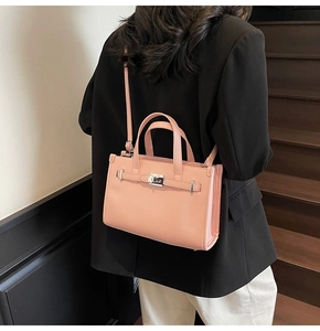 Détail du sac bandoulière en cuir litchi rose avec fermoir argenté porté par modèle