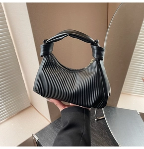 Detail view of black pleated dumpling bag with knotted handle and golden zipper closure