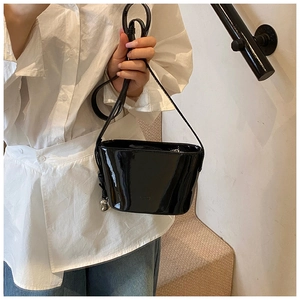 Détail d'un sac seau en cuir verni noir avec un charmant pendentif sphérique argenté