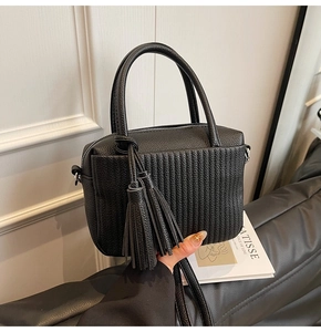Detailed view of black litchi grain leather crossbody bag with pleated texture and tassel