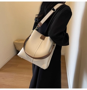 Detail of minimalist cream bucket bag featuring wide shoulder strap and brown trim detail