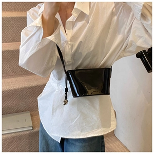 Détail d'un sac bandoulière en cuir noir brillant avec breloque sphère argentée