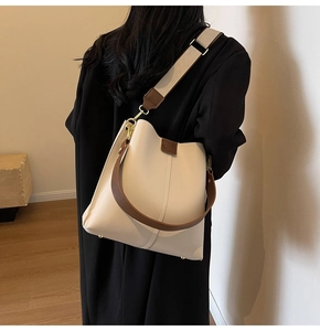 Model wearing a minimalist beige bucket bag with a brown strap in a minimalist room