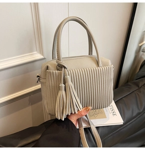 Détail du sac en cuir plissé gris avec pompons décoratifs et fermeture éclair métallique