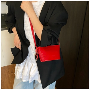 Détail d'un sac carré en cuir verni rouge avec pendentif coeur et bandoulière fine