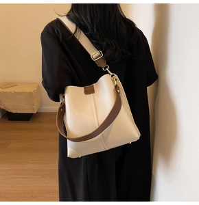Detail of cream bucket bag with brown wide strap showing the leather texture and stitching